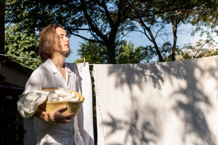 Young long hair man with closed eyes enjoying the summer sun on his face while hanging out the linen washingの写真素材