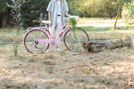Cropped side view of unrecognizable young fashinable man holding a pink bicycle with a wicker basket and plants hangingの写真素材