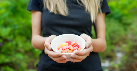 Closeup view of unrecognizable woman in black holding colorful plenty of candy in a white bowl on blurred natural green backgroundの写真素材