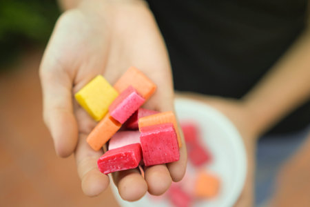 Super closeup view of yellow, red, orange and pink unhealthy candies shown by woman hand. Sugar and cavities kids health problems conceptの写真素材