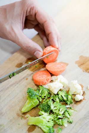 Vertical top view of mix vegetables being chopped on a wooden cutting board in the kitchenの写真素材