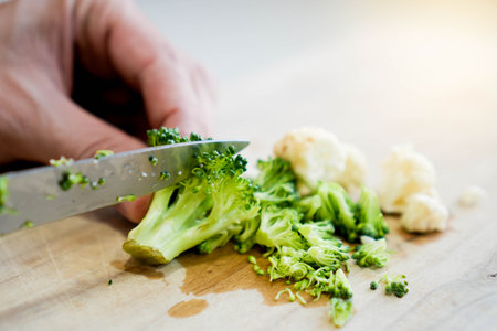 Close up selective focus view of Broccoli and cauliflower being cut with a knife on a wooden cutting boardの写真素材