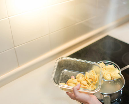 Top view of cheese tortellini pasta dumplings being boiled in water and pouring into glass containerの写真素材