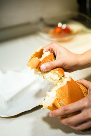 Vertical view of female hands breaking into pieces a loaf of bread on the white kitchen counter top.の写真素材