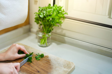 Close up view of young person hand cutting chopping fresh bunch parsley in water in the kitchen counter topの写真素材