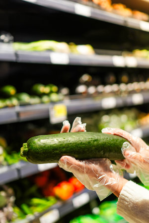 Vertical view of zucchini in female hands showing to camera in blurred supermarket backgroundの写真素材