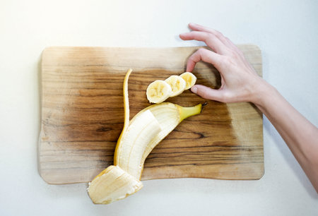 Top close up view of ripped banana cut in slices for breakfast bowl on top of a wooden cutting boardの写真素材