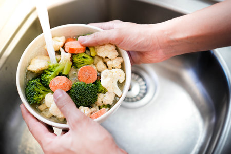 Top view of raw vegetable bowl being washed in a sink held by man in the kitchen. Vegan and healthy vegetarian foodの写真素材