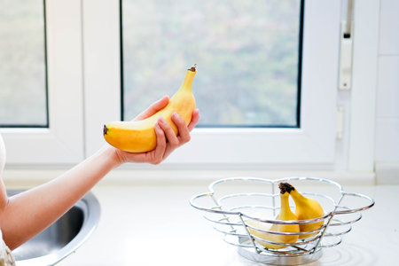 Woman's hand holding banana, snack and healthy concept. Selective focus on hands with blurred background and copy spaceの写真素材