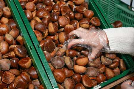 Closeup view of female hand choosing chestnuts in the store from a pileの写真素材