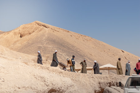 LUXOR, EGYPT - 27 Dec 2022. Group of local arab muslims working in the desert digging the sand in mountain under blue skyの写真素材