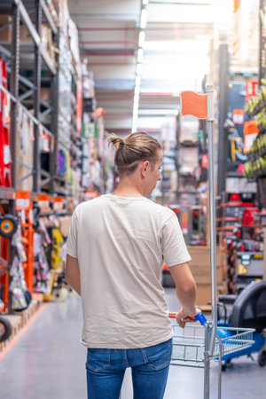 Vertical view of young man pushing a shopping cart in the corridor of an industrial hardware store with blurred backgroundの写真素材