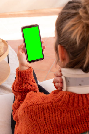 Unrecognizable female with cervical collar on neck discussing problems with doctor while having video conversation on smartphone during online session at homeの写真素材