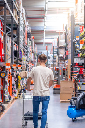 Young man on a bun buying and walking throw the middle of the aisle of a hardware store with a trolley in handsの写真素材