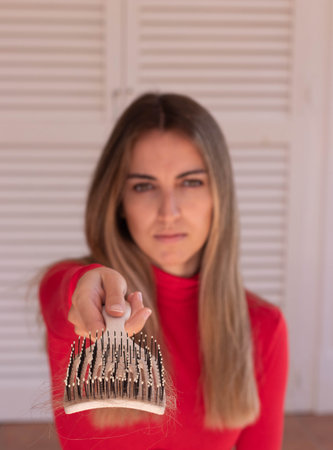 Vertical view of blurred young woman on red showing the hair brush full of hair with selective focusの写真素材
