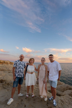 Family Bonding at Sunset: Vertical Shot of a Family of Four, Two Adults and Two teenagers, Standing on a Rocky Cliff Overlooking the Ocean at Sunsetの写真素材
