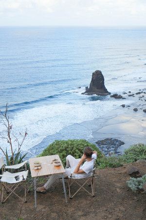 A tranquil moment of solitude, as an individual gazes upon the oceans gentle waves and a distant rock formationの写真素材