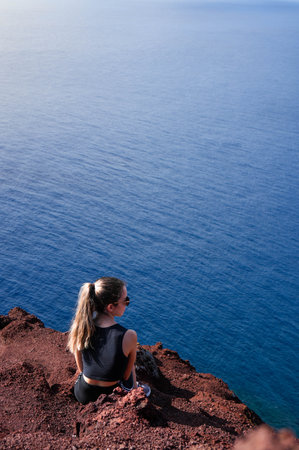A mesmerizing photograph of a woman finding solace and tranquility, sitting atop a cliff overlooking...