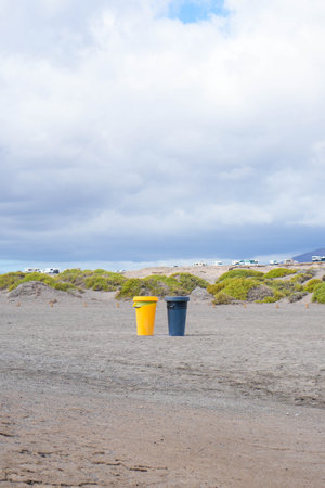 Two vibrant garbage cans stand out against the muted colors of the sand and cloudy sky at a beach, promoting environmental cleanliness.の写真素材