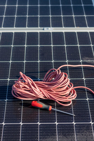 Vertical top view of red cable reel and a screwer leaning on a solar panel installation for new...