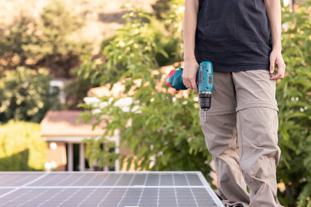 Cropped view of young woman working on a solar panel power plant holding an electric screwdriver while walking standingの写真素材