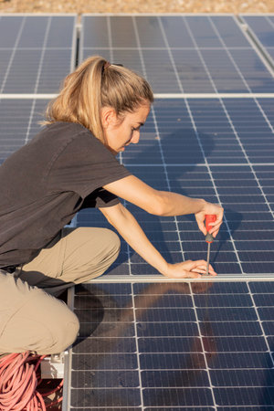 Top view of young woman screwing a screw to assemble the photovoltaic solar panels on the roof of a house as green energy conceptの写真素材