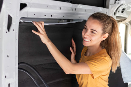Portrait of happy smiling woman sticking the rubber isolation on the wall in the self made camper van conversionの写真素材
