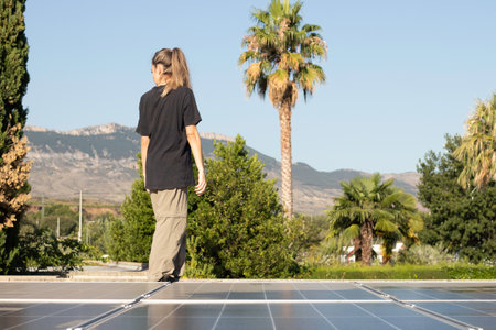 Front view of young woman worker standing looking to the back with vegetation in the background and solar panels on the sideの写真素材