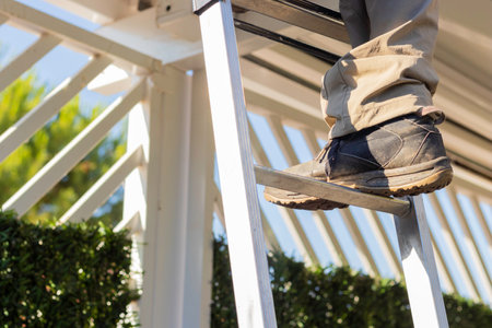 Close up view of faceless person climbing the ladder while working on the roof of a house. Security shoe at work concept with lightの写真素材