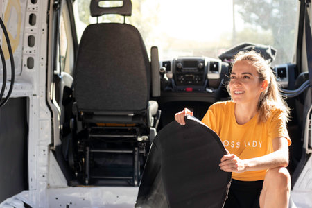 Happy smiling young woman holding rubber insulation for a camper van built conversion with copy space and bright backlightの写真素材