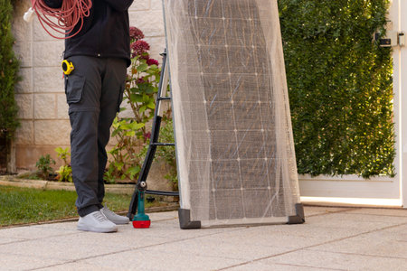 Cropped view of unrecognizable young man electrician worker with a solar panel, wire and stairs on the side outsideの写真素材