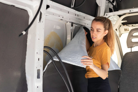 Young woman concentrated looking to the self adhesive rubber insulation about to be glued to the van wall in a camper van conversionの写真素材
