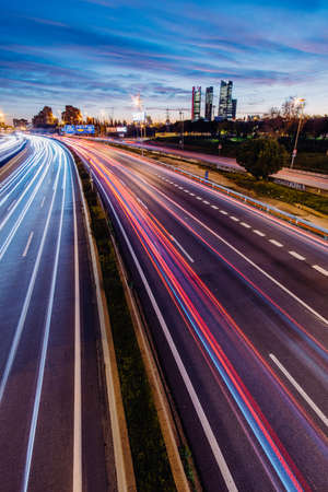 Highway A-1in Madrid Spain with car light trails at rush hour at sunset with Cuatro Torres Business area in the background. Blue tones in the sky in vertical.の写真素材
