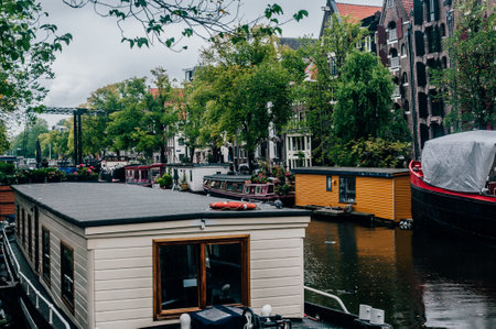Several houseboats in Amsterdam The Netherlands in a cloudy day with the canal and water reflections with trees and brick housesの写真素材