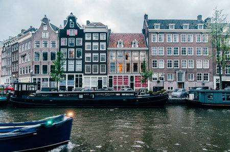 Classic houses located in a canal in Amsterdam The Netherlands with houseboats and a moving boatの写真素材