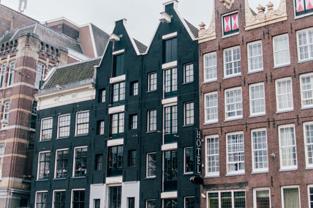 Classic dutch buildings and hotel in Amsterdam, The Netherlands, build with brown and black bricks with many open windows. Cloudy day.の写真素材