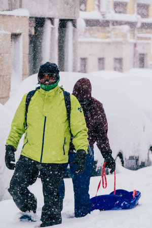 Madrid, Spain - January 2021: two people with snowshoes, snow goggles and a sled in a street in the capital of Spain covered in snow due to Filomena Storm.のeditorial素材