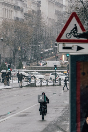Madrid, Spain - January 2021: Deliveroo (food delivery company) rider in Alacala street with hevy snow due to Filomena Storm. Picture from behind with bus in the back.のeditorial素材