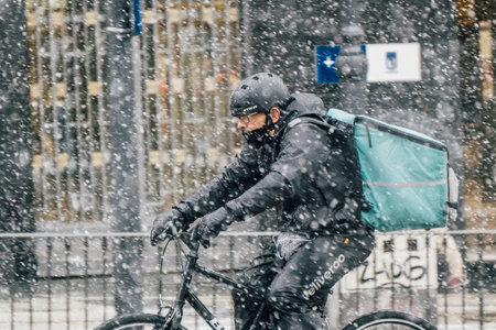 Madrid, Spain - January 2021: Deliveroo (food delivery company) rider in Alacala street with hevy snow due to Filomena Storm. Picture from the left, rider on bike.のeditorial素材