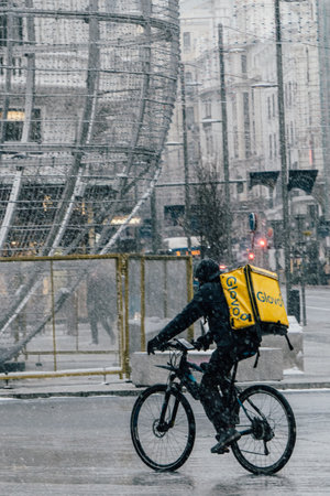Madrid, Spain - January 2021: Glovo (food delivery company) rider in Alacala street with hevy snow due to Filomena Storm. Christmas lights in the background. View from the left.Rider on bike.のeditorial素材