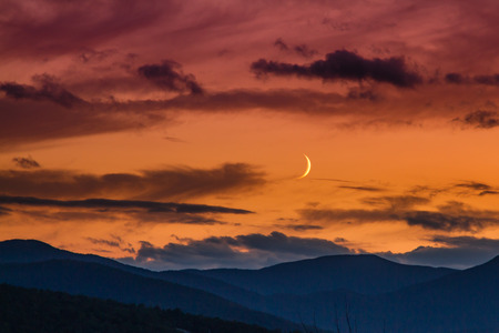 A crescent moon hovers over the Appalachian Mountains  in Sundy River, Maine during sunset.の写真素材