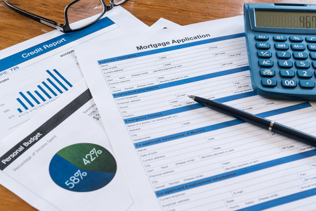 Mortgage application on desk with credit report, budget, calculator, pen and glasses