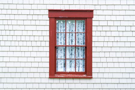 Old rustic red window frame on cedar shingles with weathered peeling