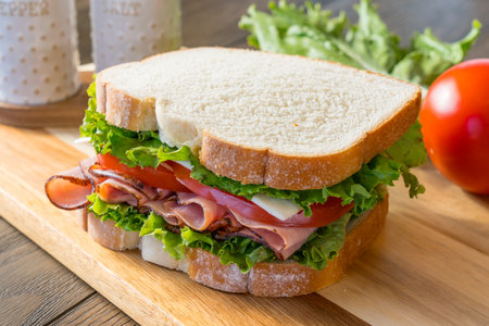 Fresh ham, tomato and cheese sandwich on cutting board