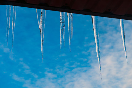 Ice icicles hanging from the edge of the roof against the blue sky.