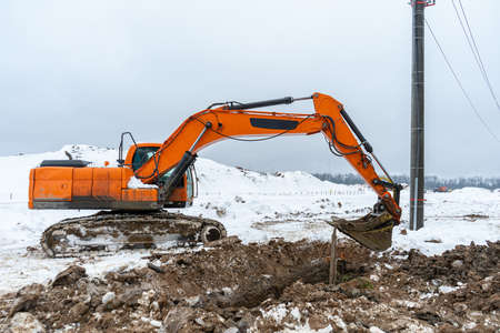 A large orange excavator digs the ground to repair and lay underground utilities and cables for electricity and communicationsの写真素材