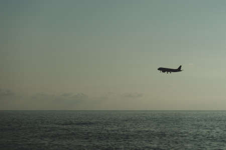The silhouette of the plane flies against the background of the sky and the sea, imitation of film photography.の写真素材