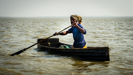 Ishwardi, Bangladesh - 10.10.2022: poor Bengali man in a makeshift boat floats down the Ganges river. Fisherman in a boat in the middle of the river.のeditorial素材