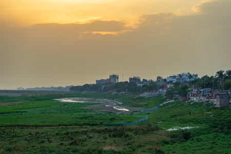 serene sunset over rural landscape with buildings on right and open fields in foreground, creating a...