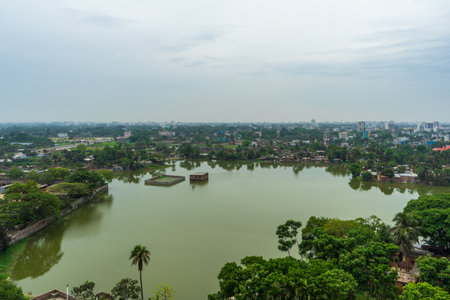 Aerial view of green cityscape with large lake, buildings surrounded by trees under cloudy skyの写真素材